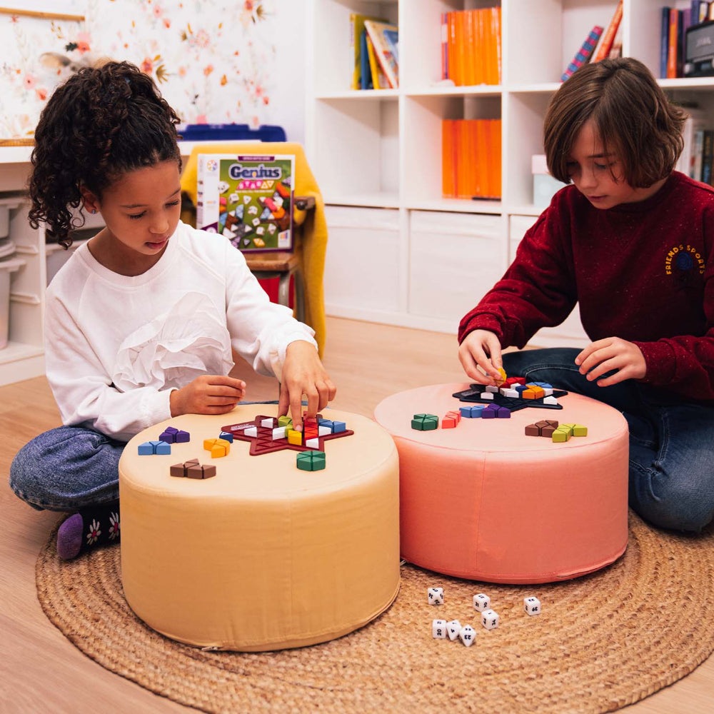 Smart Games Genius Star puzzle game; two kids play on pastel round ottomans with colorful tiles.