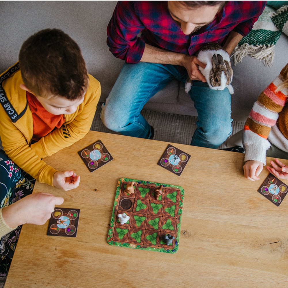 Smart Games Grabbit puzzle game; brown grid board with green leaf tiles, children playing around
