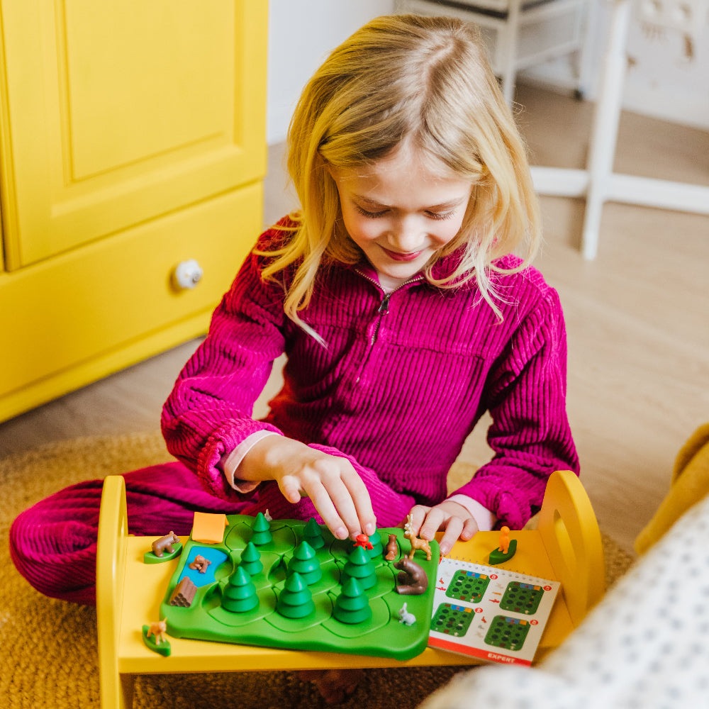 Smart Games Grizzly Gears educational board game; child plays with green tree pieces on a yellow table.