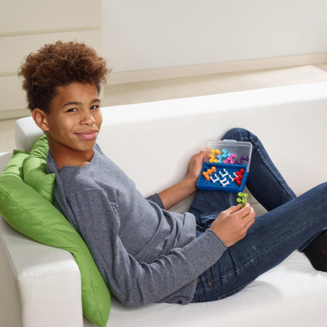 Smart Games IQ Blox educational toy set with colorful blocks in a blue tray, boy lounging on sofa