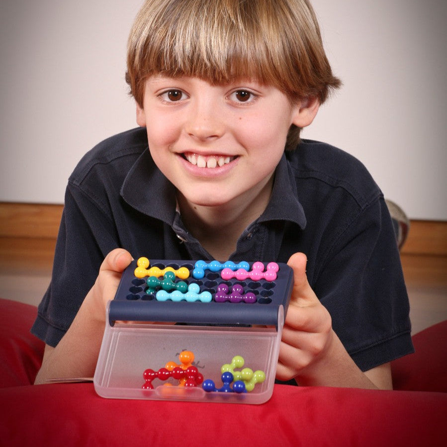 Smart Games IQ Fit puzzle game with colorful pegs in a blue case, smiling child playing.