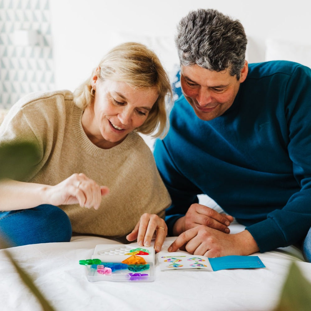 Smart Games IQ Love puzzle game for couples, featuring colorful tiles and challenge cards, being played on a bed