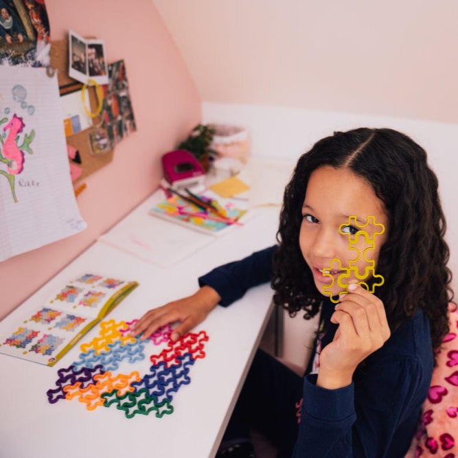Smart Games IQ Matrix puzzle toy; child holds yellow interlocking piece with colorful pieces on the desk.