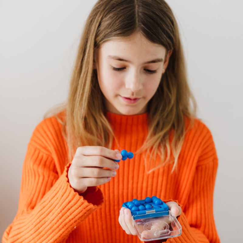 Smart Games IQ Mini puzzle game with blue pegs in a blue case being held by a girl