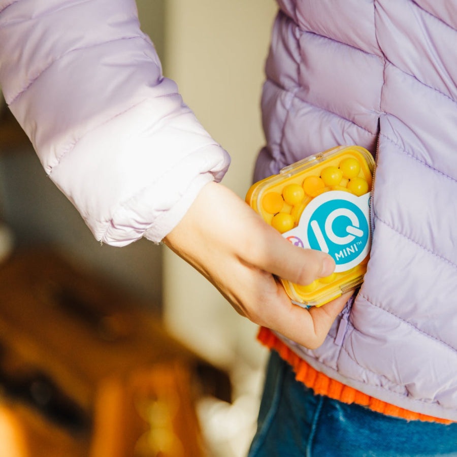 Smart Games IQ Mini educational toy capsule with yellow beads, held by child in lavender jacket