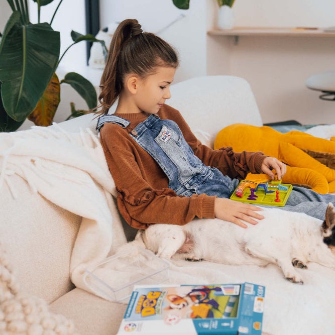 Smart Games Smart Dog Obstacle Run puzzle toy; child sits on sofa with colorful game board and a dog nearby