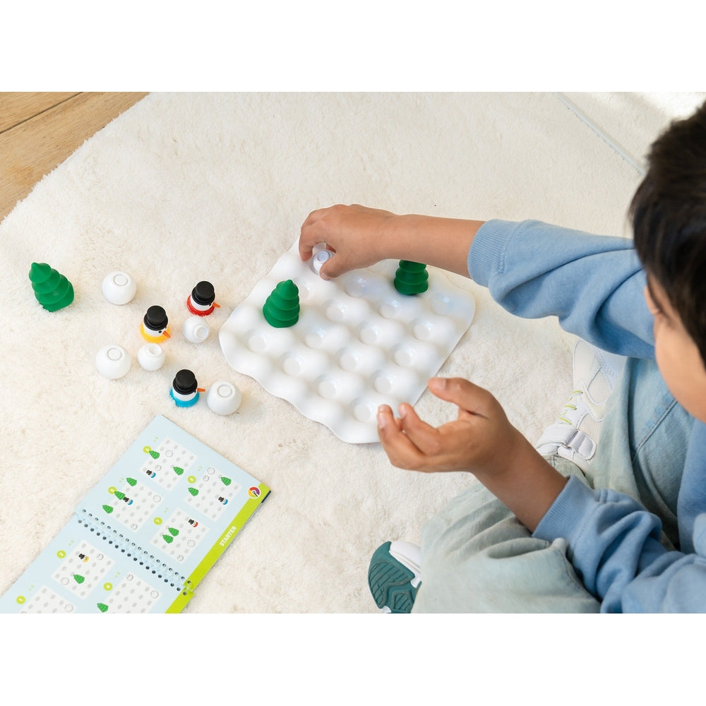 SMART GAMES Snow Problem: child places white pegs around green trees on a white pegboard, a wintery puzzle toy.