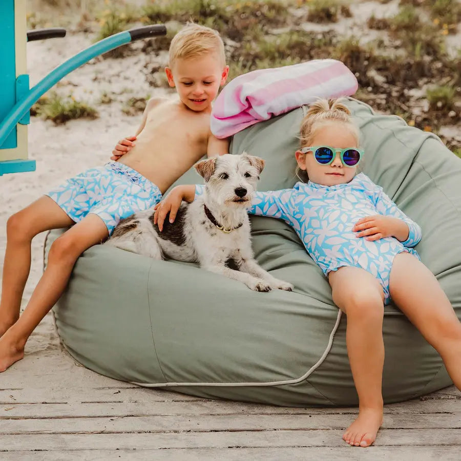 Snapper Rock Aqua Bloom Volley Board Short worn by two kids lounging on a beach in blue floral swimwear.