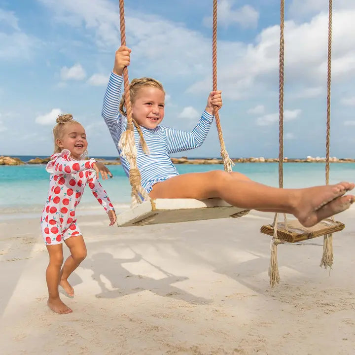 Snapper Rock Cornflower Stripe Surf Suit toddler swimsuit, blue/white stripes, girl swinging on a rope swing at the beach.
