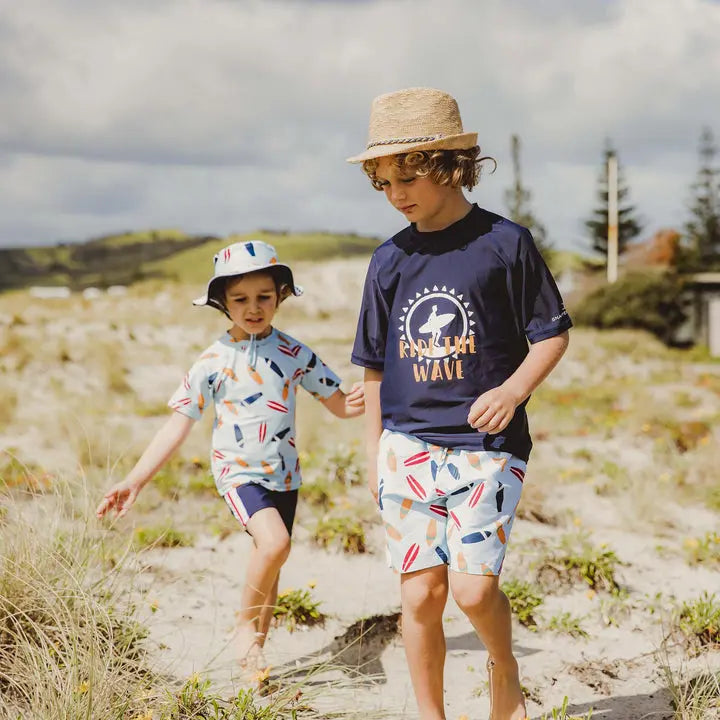 Snapper Rock Retro Surf Baby Set: navy tee with logo and surf-print shorts on two kids at the sunny beach.