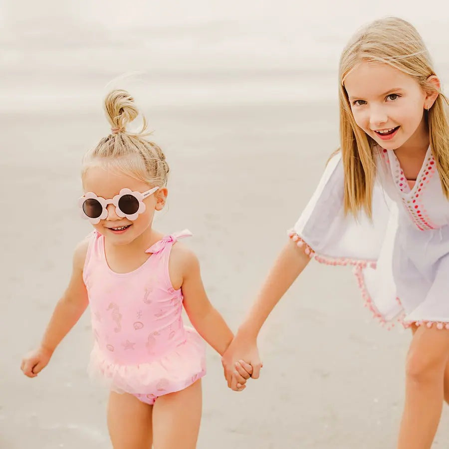 Snapper Rock Seahorse Sparkle Skirt Swimsuit, pink toddler one-piece with a frill skirt, shown as two girls walk hand-in-hand on the beach.