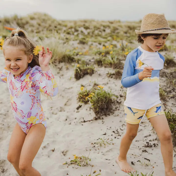 Snapper Rock Sunrise Shark Baby Set: floral long-sleeve swimsuit and blue-yellow rash guard, two kids playing on sunny beach.