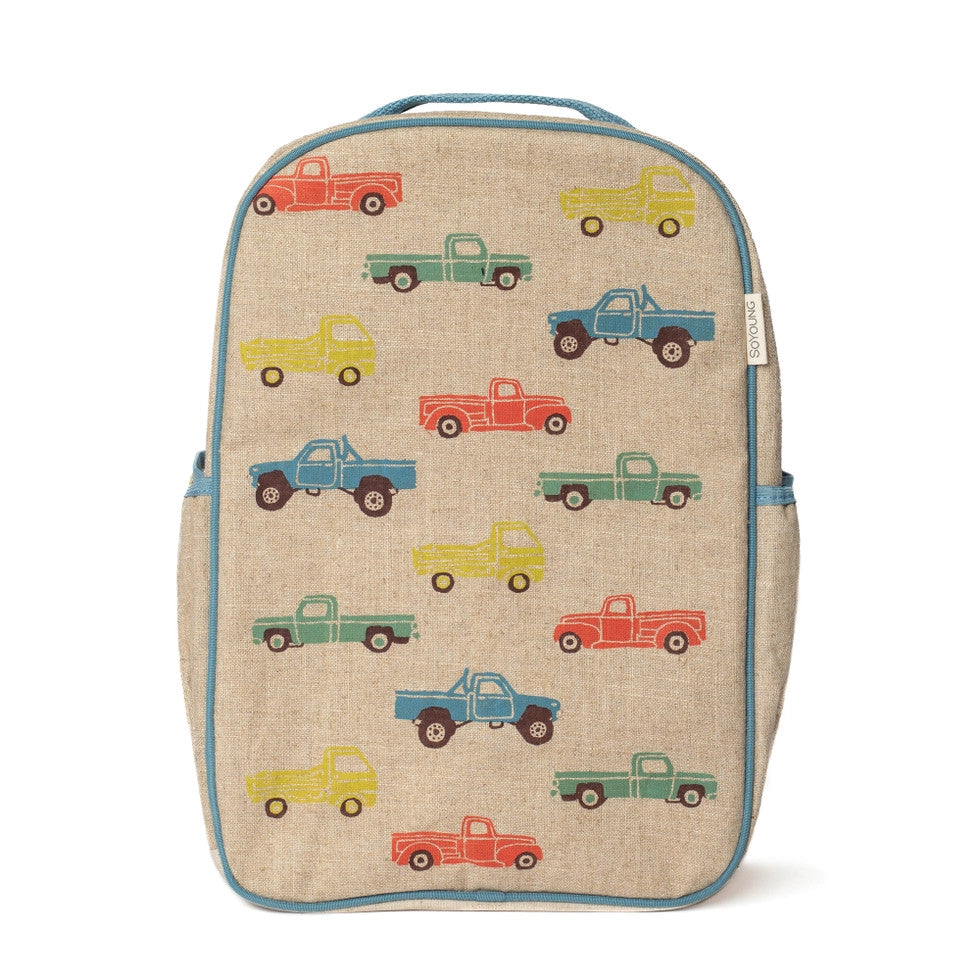 So Young Grade School Backpack in beige burlap with multicolor trucks; blue trim and side pockets visible.