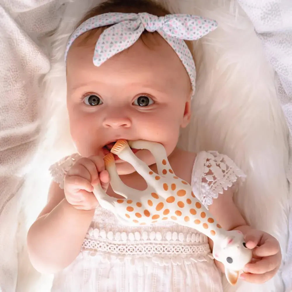 Sophie la Girafe teether held by baby in white lace dress and pastel headband