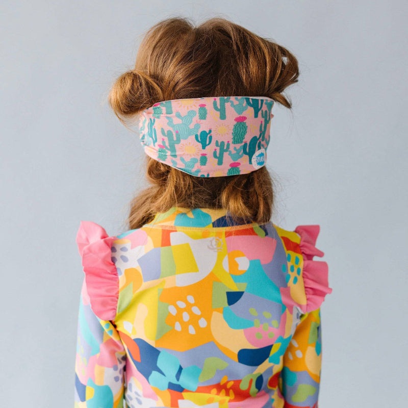 Splash Swim Goggles Desert Sunshine headband with pink cactus print worn by a child in a bright colorful ruffle dress