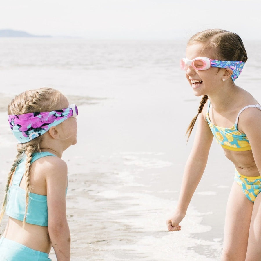 Splash Swim Goggles Flamingo Pop, pink and blue pattern, worn by two girls at the beach