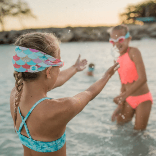 Splash Swim Goggles Mermaid; two kids in bright swimsuits playing in shallow water, mermaid headbands visible.