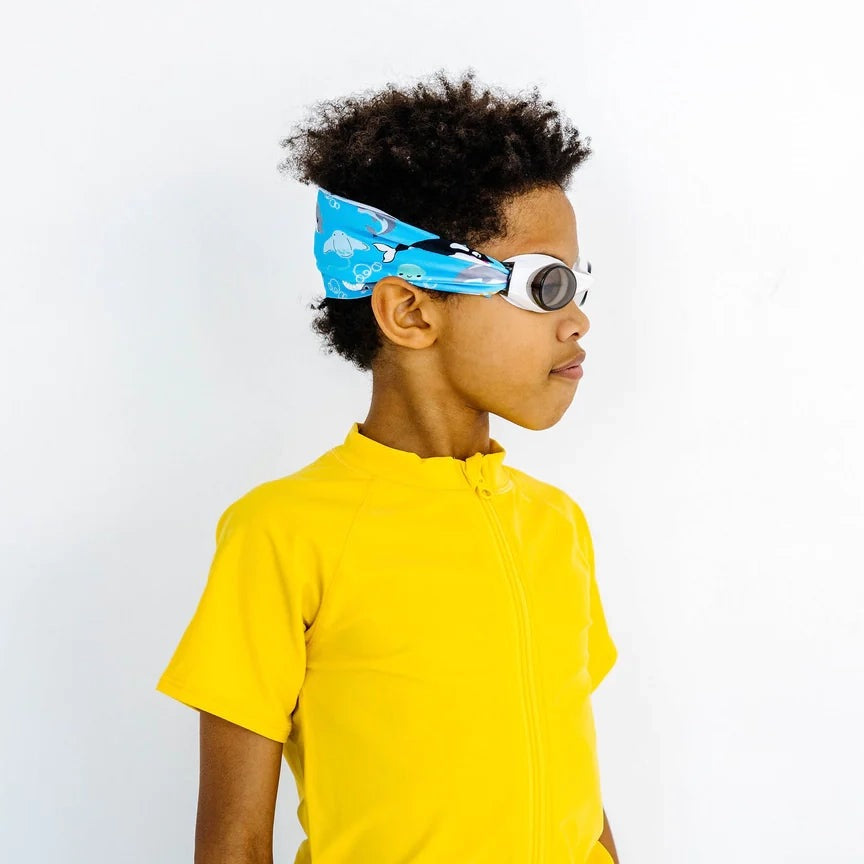 Splash Swim Goggles Ocean Friends for kids, white goggles with blue ocean-pattern headband on a young swimmer in a yellow shirt.
