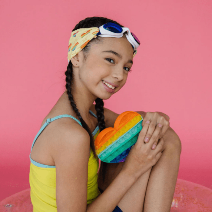 Splash Swim Goggles Rainbow Pop worn by girl in yellow swimsuit holding rainbow pop toy