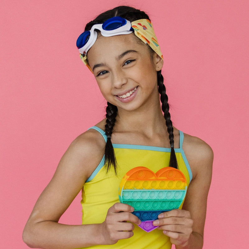 Splash Swim Goggles Rainbow Pop; white-framed goggles with blue lenses, rainbow heart pop toy held by a smiling girl.
