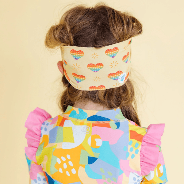 Splash Swim Goggles Rainbow Pop worn by child with rainbow-heart headband and bright color-block swimsuit.