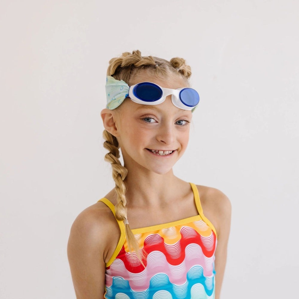 Splash Swim Goggles Sea Glass kid size with white frame and blue lenses worn by a girl in a colorful swimsuit