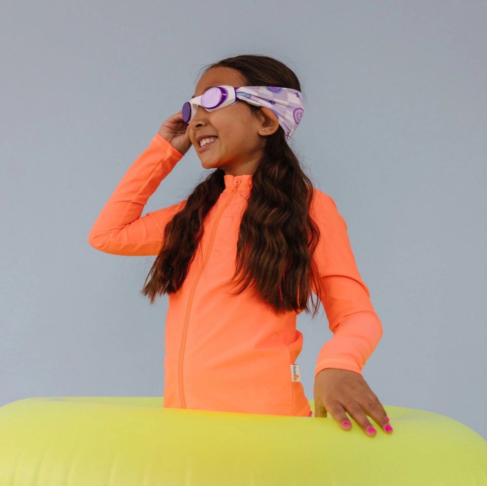 Splash Swim Goggles Smiley worn by girl in bright orange swim top with purple headband; yellow inflatable float in foreground