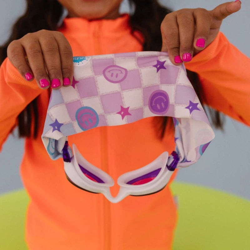 Splash Swim Goggles Smiley by SPLASH SWIM GOGGLES for kids, pink-purple printed band, held by child in bright orange outfit