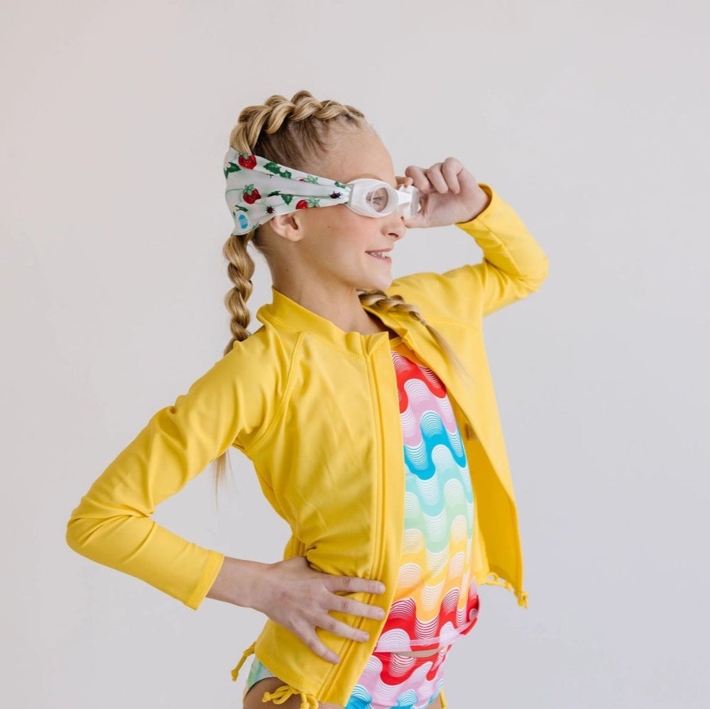 Splash Swim Goggles Strawberry Fields for kids with clear lenses and white strap, worn by girl in a rainbow swimsuit