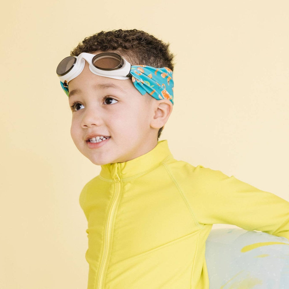 Splash Swim Goggles Surf Trip goggles, brown lenses on a child in a bright yellow swimsuit and blue printed headband