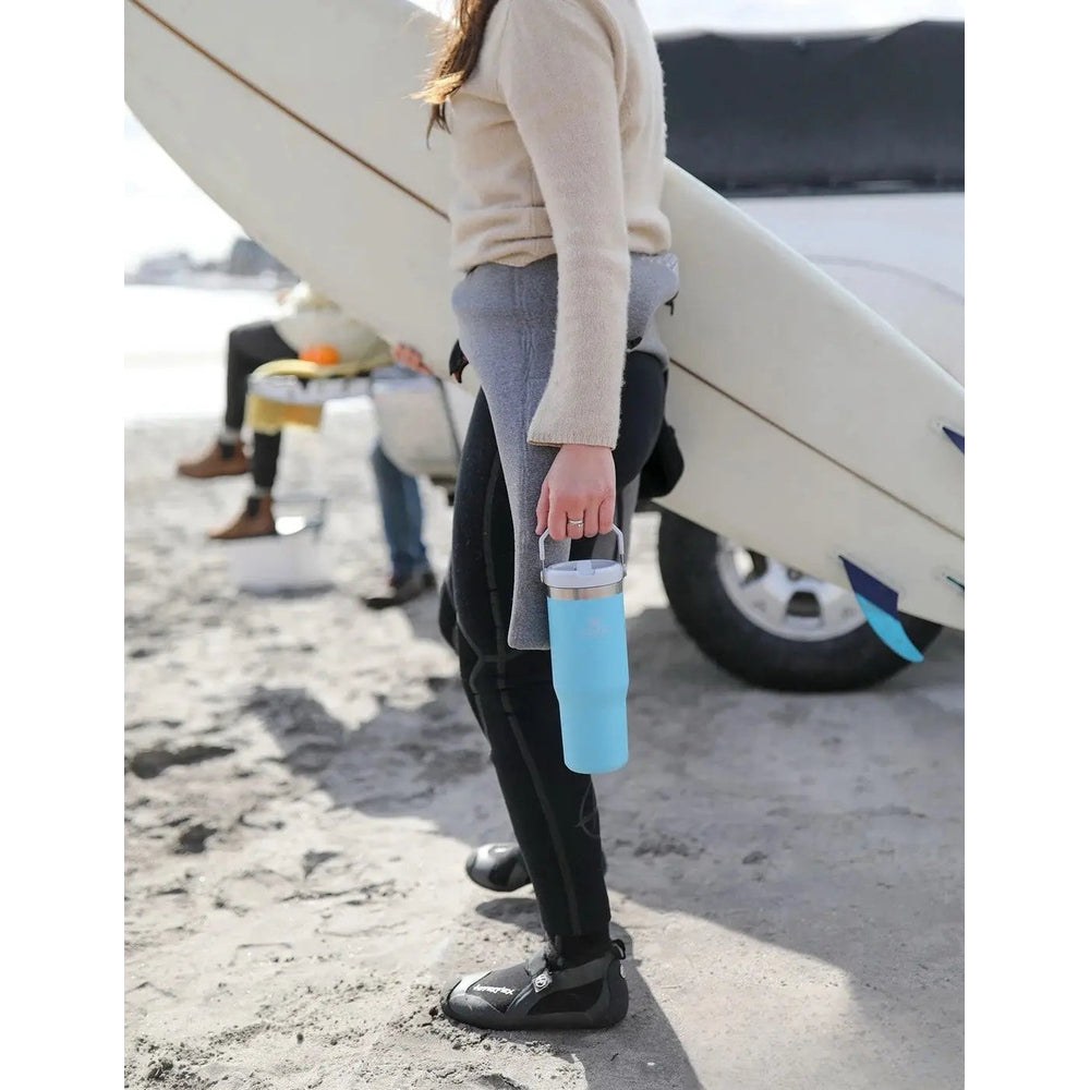Stanley The IceFlow Flip Straw Tumbler 30 oz in blue carried by a person on the beach beside a surfboard