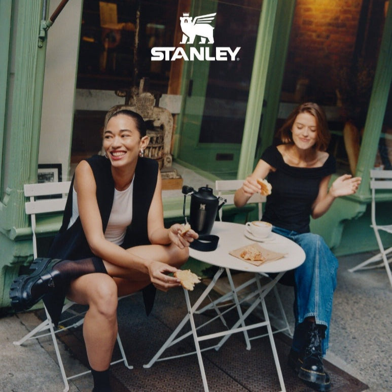 Stanley The Iceflow Flip Straw 2.0 Tumbler 20 oz, black, on a cafe table as two friends snack outdoors with a flip straw ready.