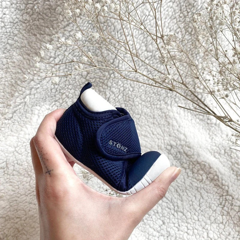 Stonz Cruiser Original Baby Shoes Black held in hand, navy mesh with white sole and Velcro strap.