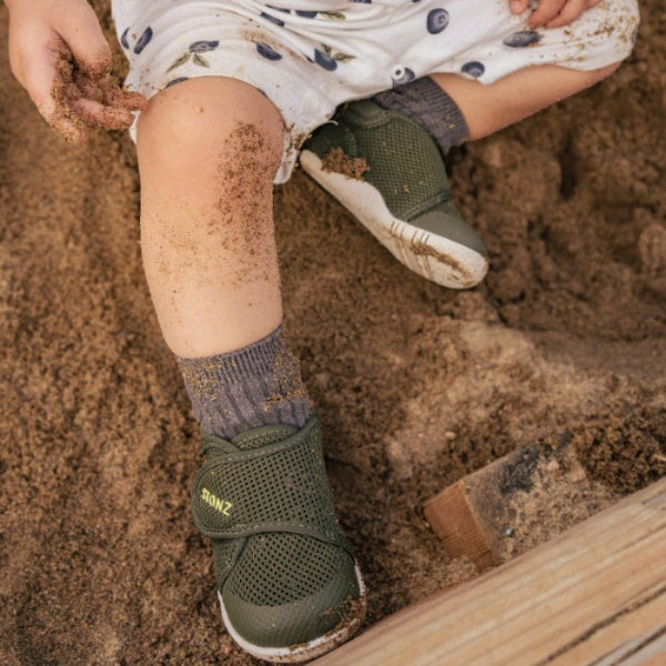 Stonz Cruiser Original Baby Shoes Cypress green mesh sandals with Velcro straps, worn by toddler in sand.