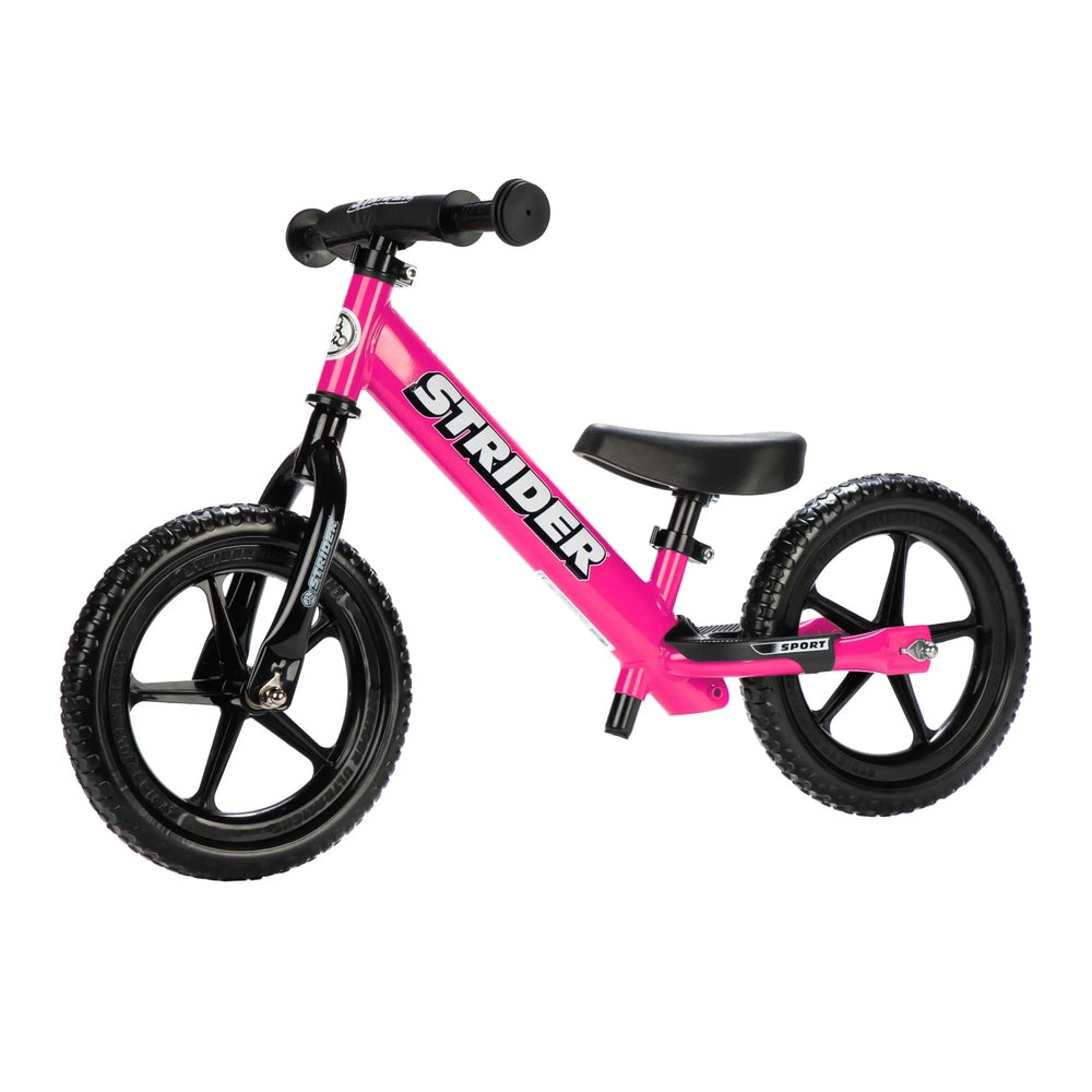 Strider 12 Sport balance bike, pink frame with black wheels and saddle, ready for balance training.