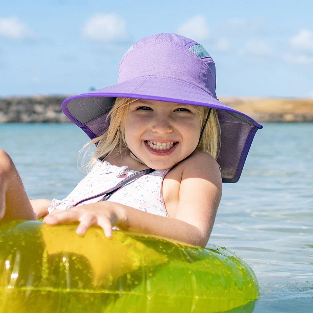 Sunday Afternoons Kids' Ultra Adventure Hat Pumice in purple; child smiles on a yellow inflatable raft under bright sun.