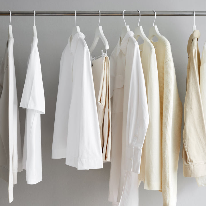 Shirts and sweaters in white and cream hanging on a metal clothing rack