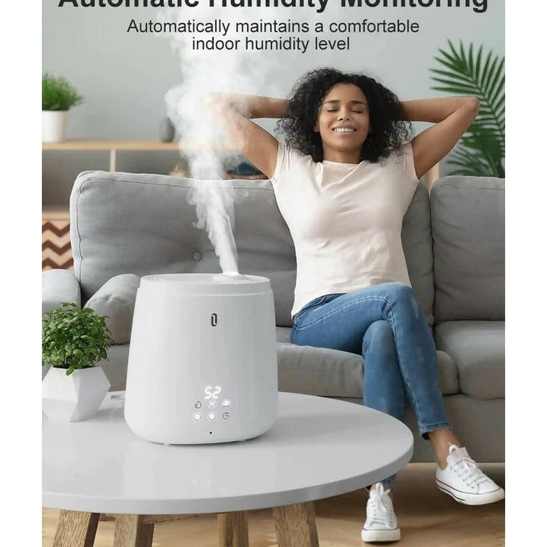 TAOTRONICS TaoTronics 6L Ultrasonic Humidifier, white, emitting mist as a woman relaxes on a sofa.