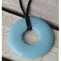 Teethease Original Pendant necklace in light blue silicone on a black cord, resting on a weathered surface