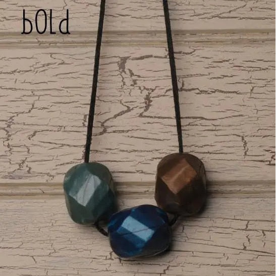 Teethease Rockease Trio teething beads on a black cord with three faceted teal, blue, brown stones hanging.