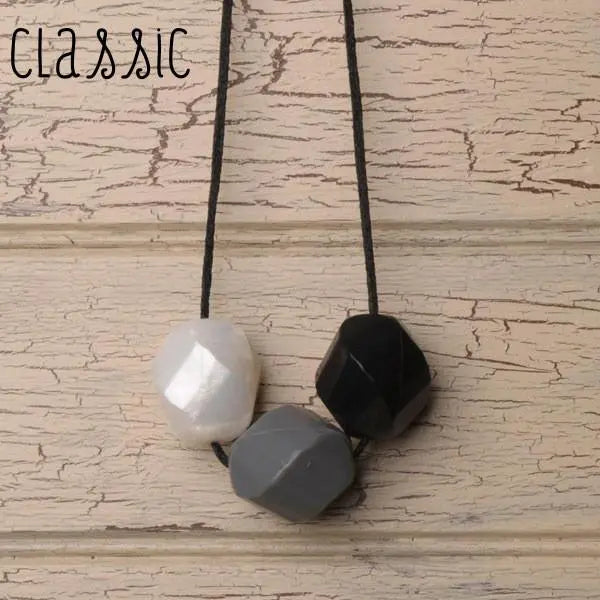 Teethease Rockease Trio beads on cords in white, gray, and black, shown as a teething necklace.