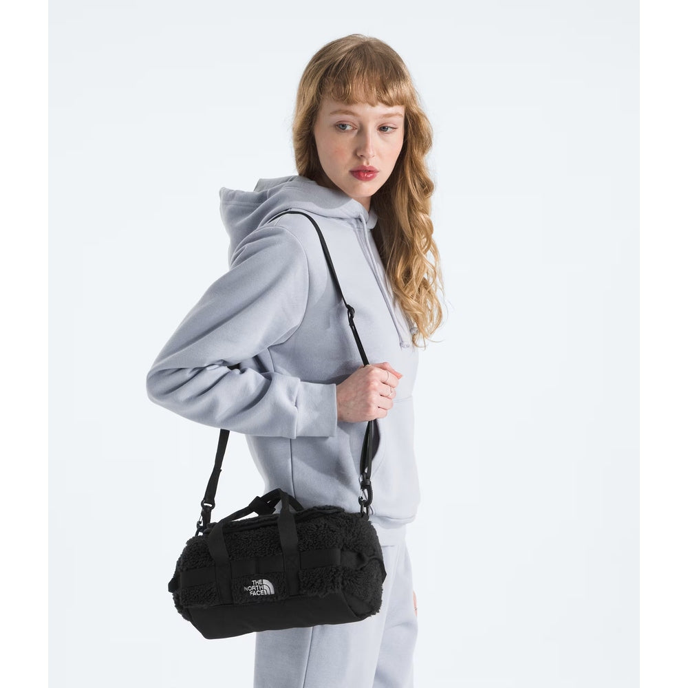 The North Face Base Camp High Pile Mini Bag in black with fleece-textured exterior, worn as a crossbody by a model in a gray hoodie.