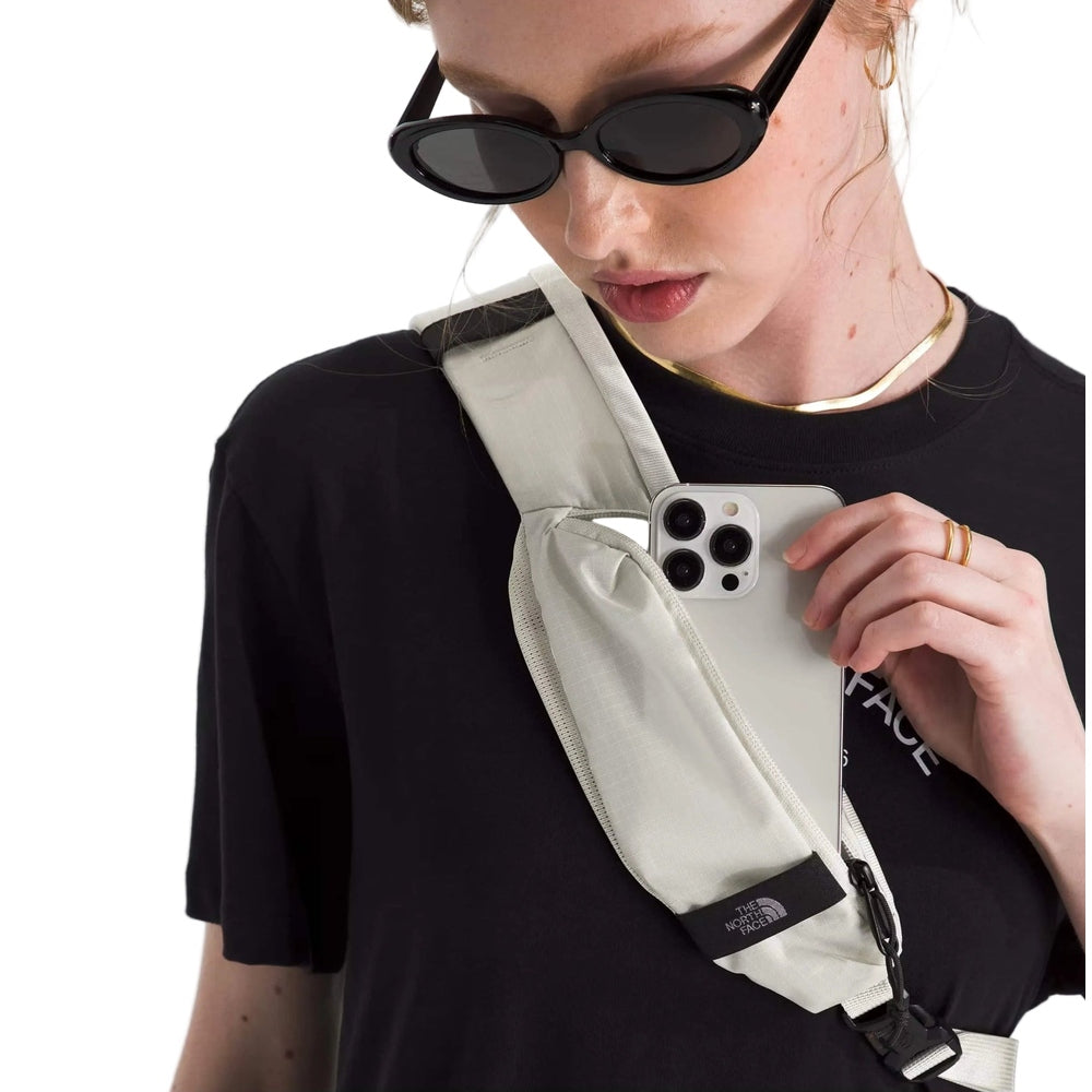 The North Face Borealis Sling Bag in Cream worn across body with phone in pocket