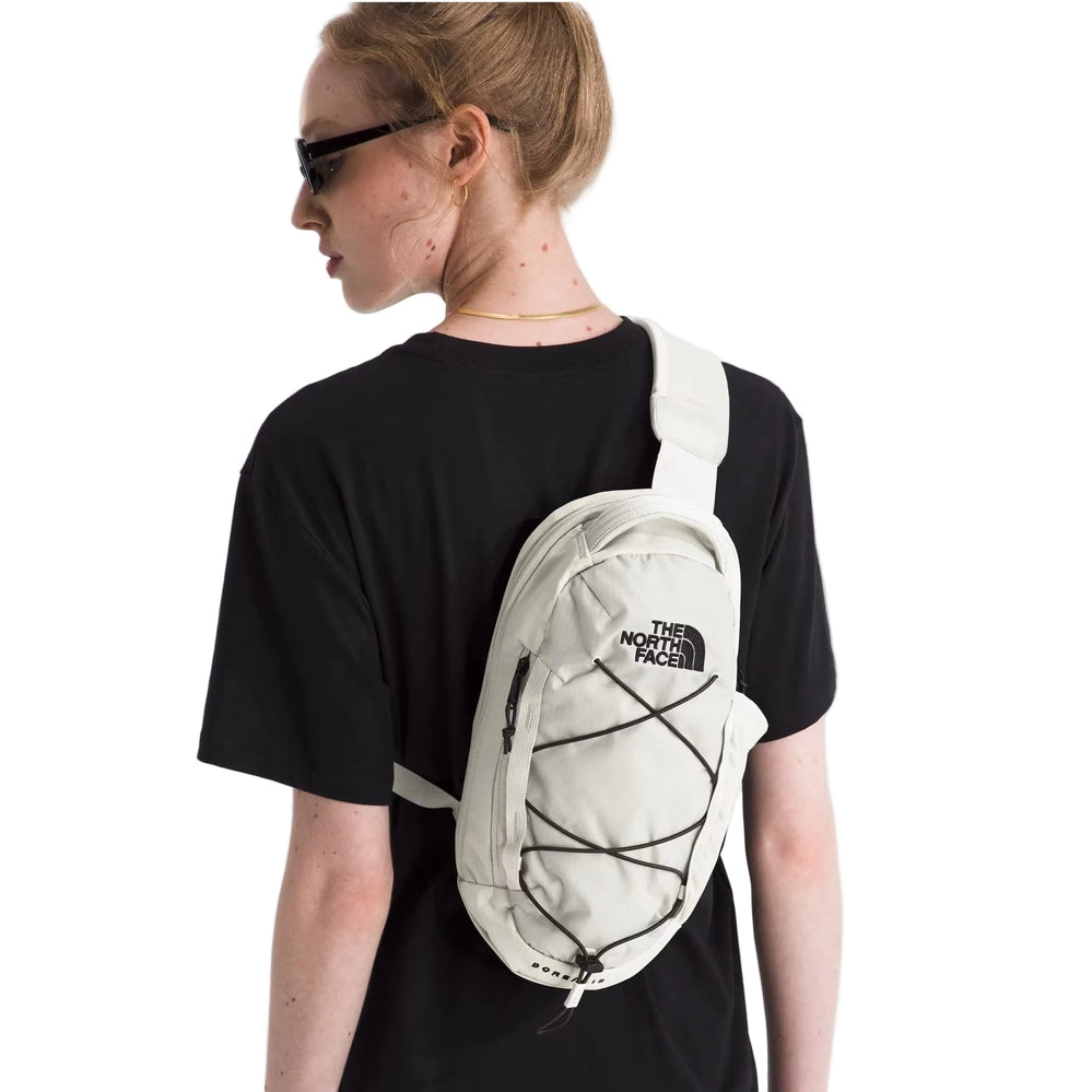 The North Face Borealis Sling in Cream White with black bungee cord front, worn crossbody.