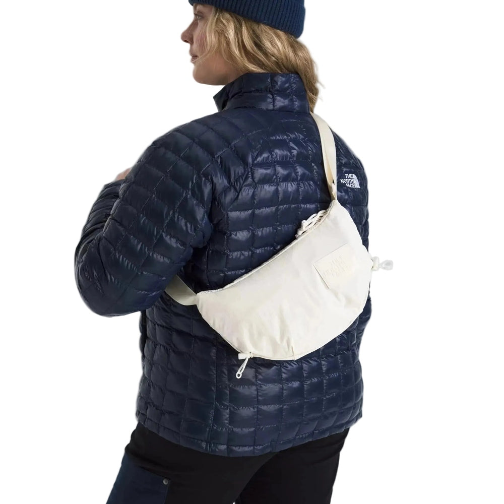 The North Face Never Stop Crossbody Bag in Cream worn across the body over a navy quilted jacket.