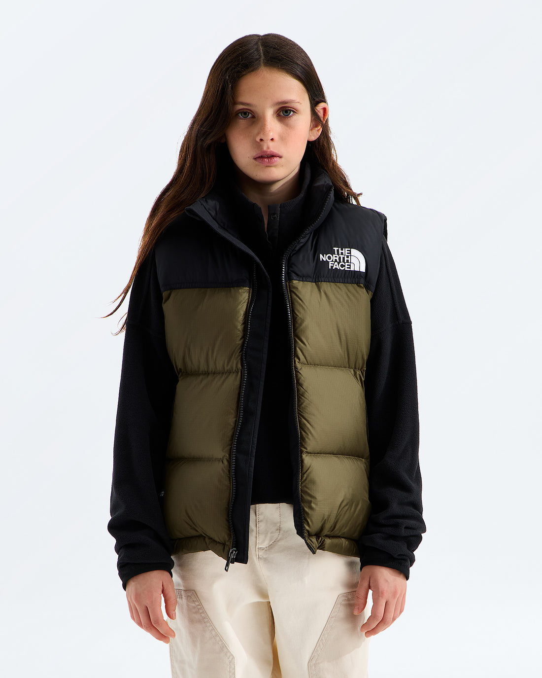The North Face kids’ 1996 Retro Nuptse Vest in Caraway Seed, front view over a black hoodie