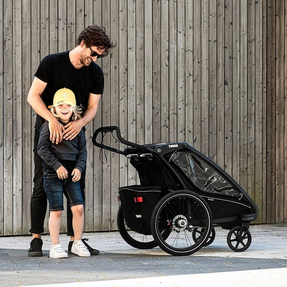 Thule Chariot Sport Multisport Bike Trailer Midnight Black with dad guiding a child beside it.