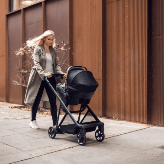 Thule Shine baby stroller with bassinet in black, pushed by a woman on city sidewalk