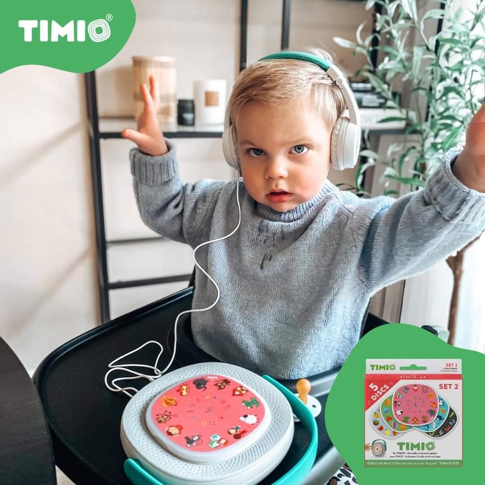 Timio Player Starter Kit with toddler wearing white over-ear headphones and pink Timio disc on a teal tray.