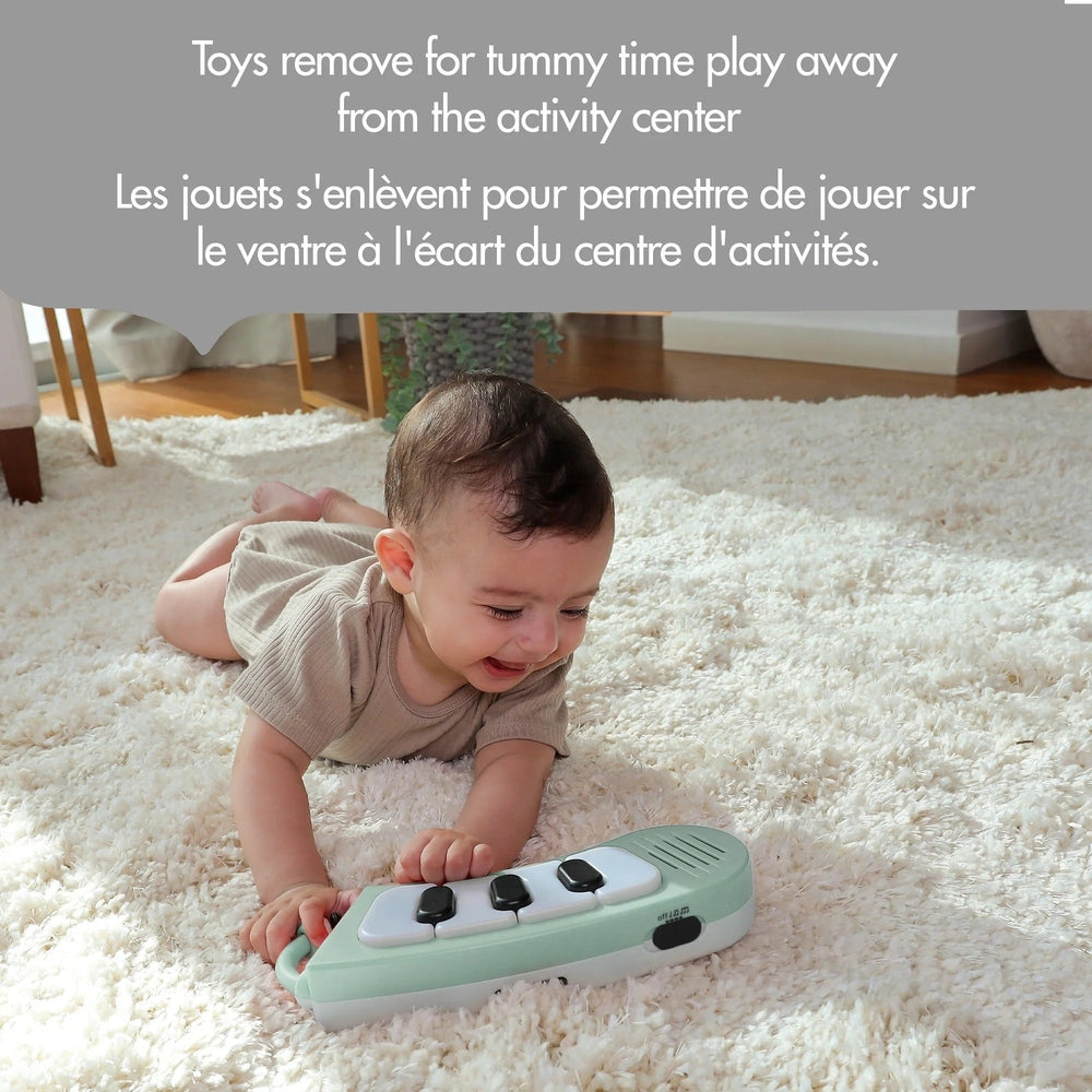 Tiny Love 5-in-1 Here I Grow stationary activity center in mint green; baby plays piano keys on a fluffy rug.
